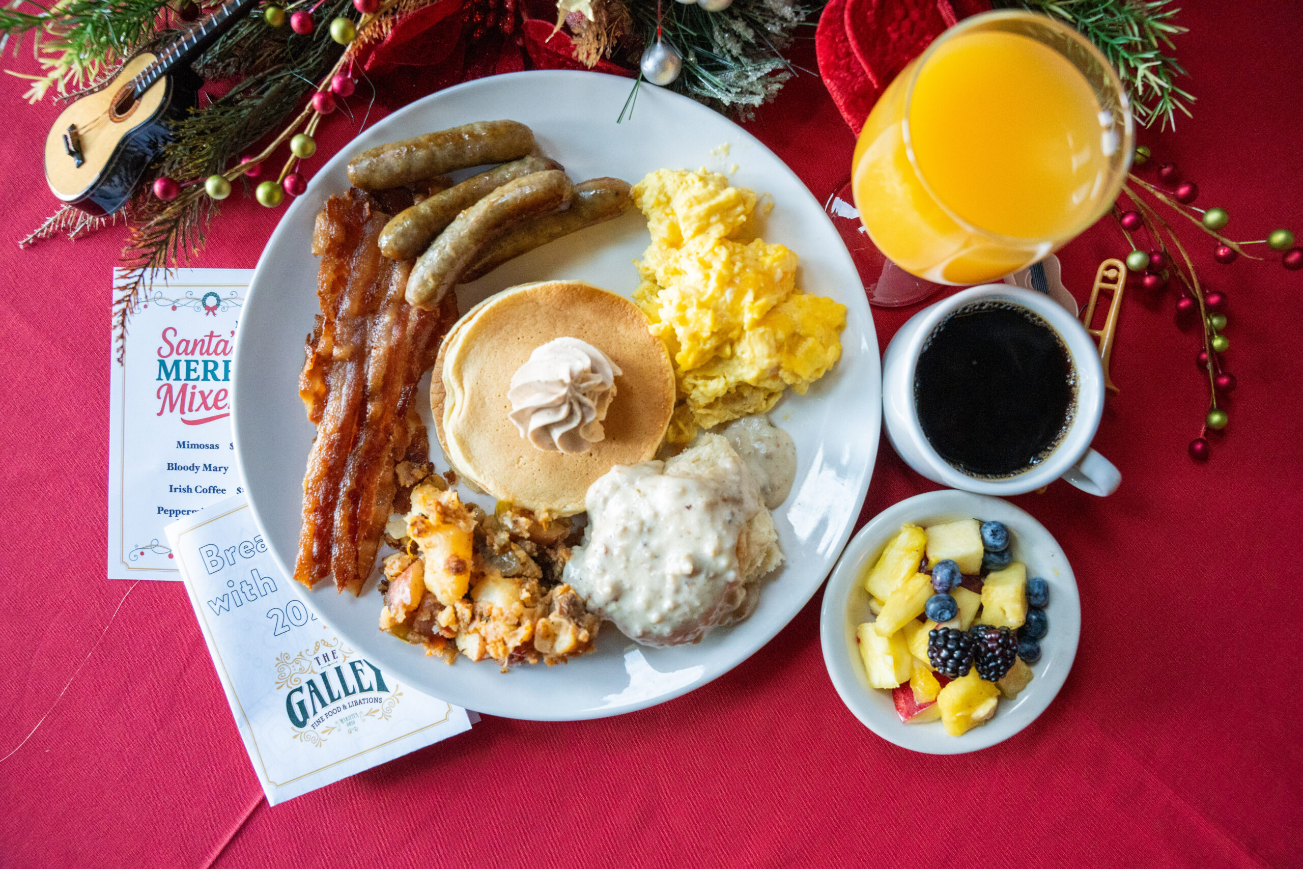 Breakfast plate with eggs, pancakes, bacon, sausage, home fries, and biscuits and gravy, with fruit, coffee, and juice